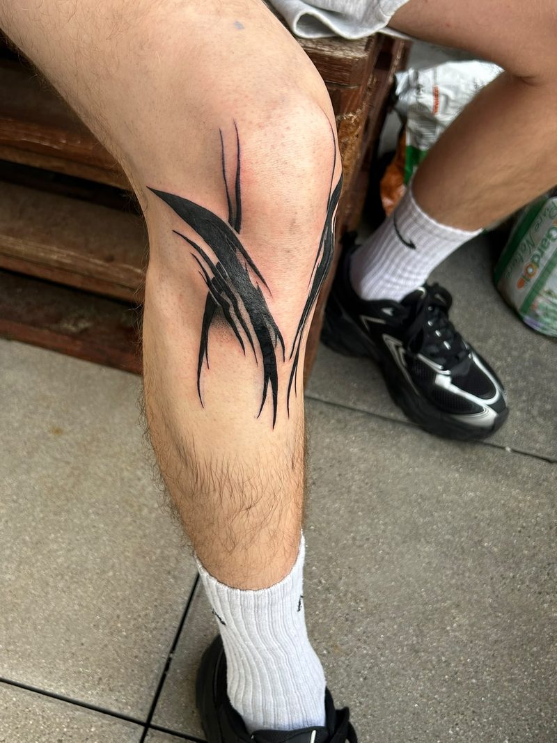 Abstract blackwork tattoo with brushstroke shapes around the knee