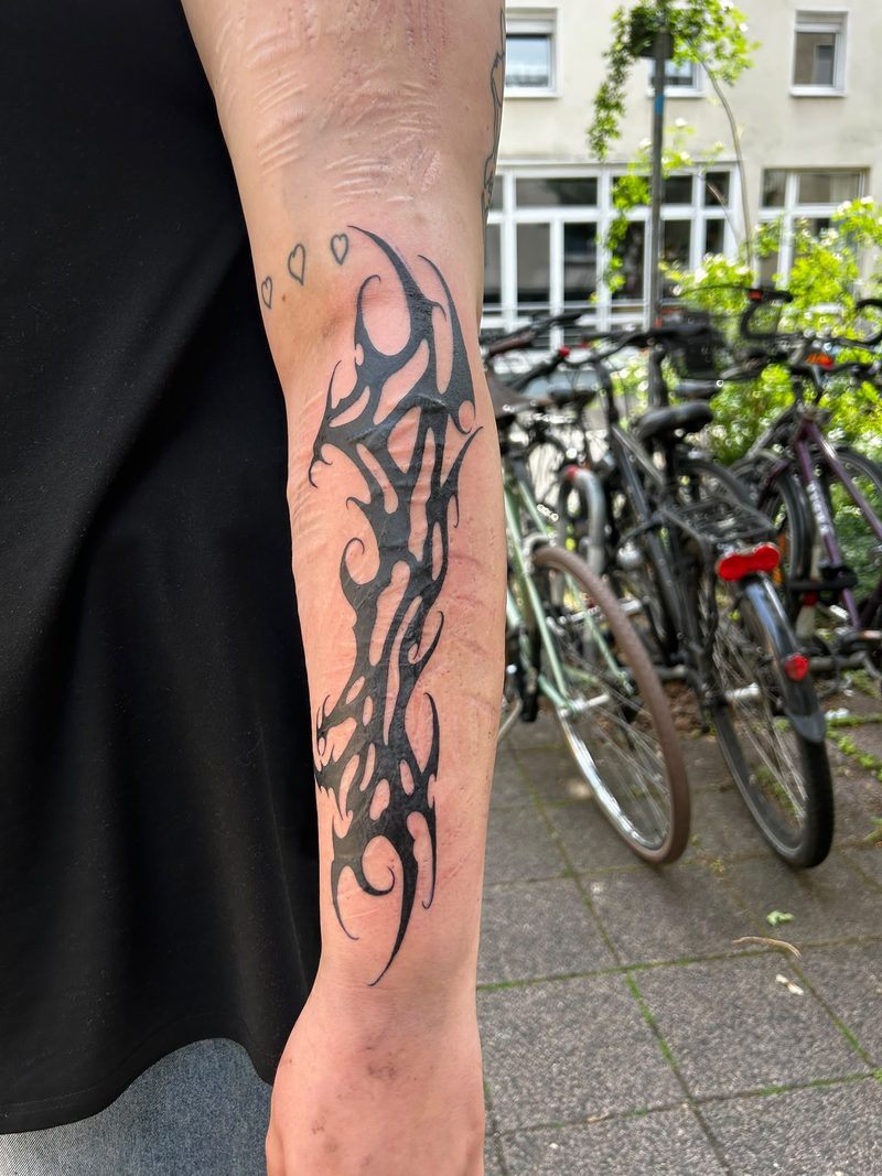 Bold blackwork ornament on the forearm with small fine line hearts
