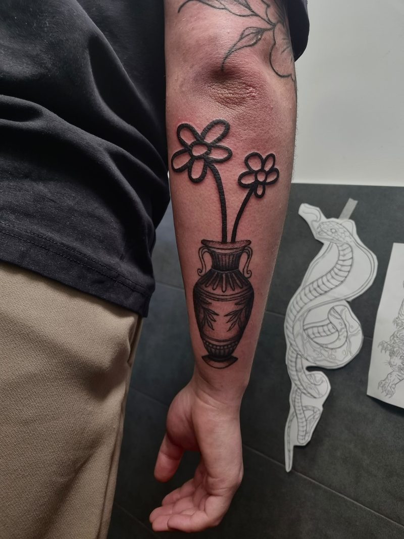 Ignorant style tattoo: naively drawn flowers in a shaded vase on the forearm