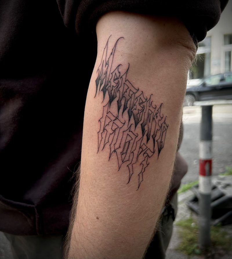 Lettering tattoo in sharp gothic script on the upper arm