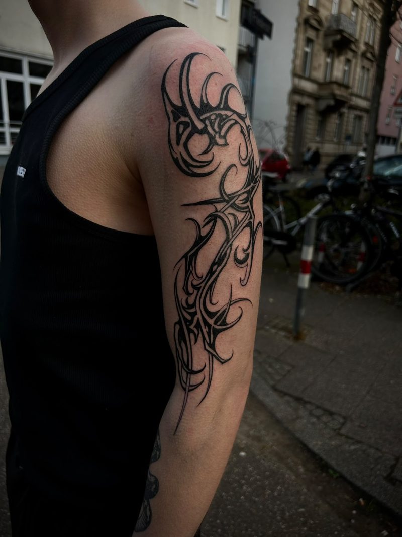 Ornamental blackwork tattoo on the upper arm with sharp, organic tapering shapes