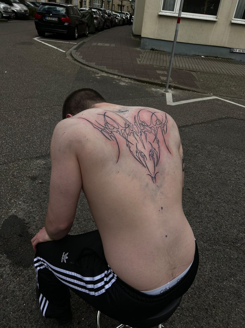 Ornamental fine line tattoo with a heart-shaped centre on the upper back