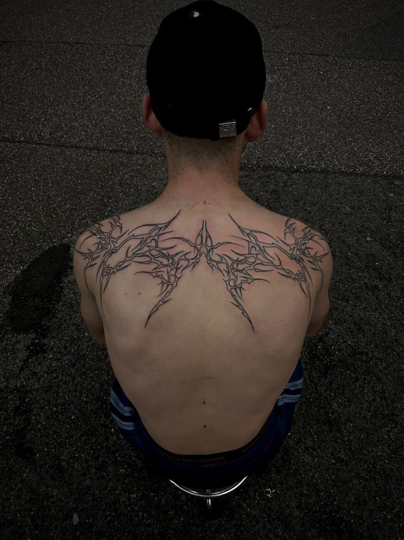 Symmetrical fine line ornamental tattoo across the shoulders and upper back